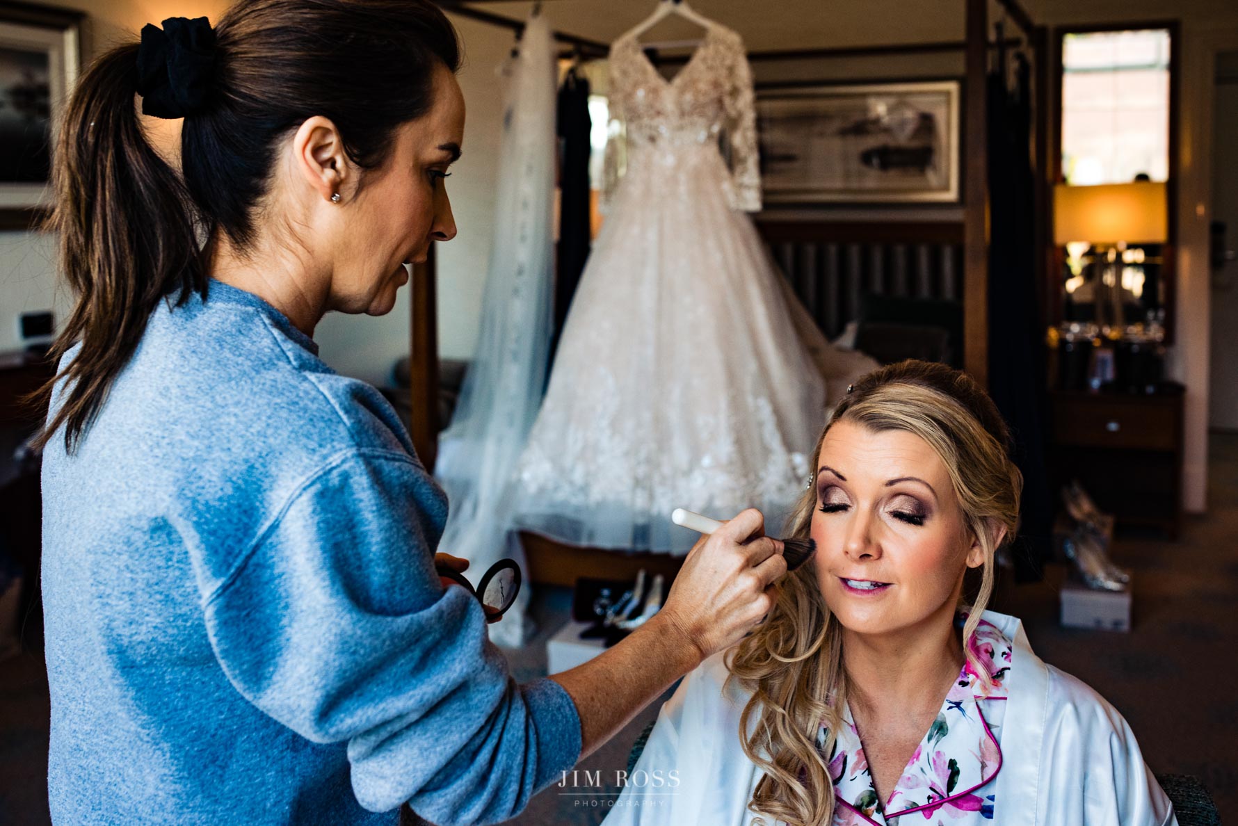 makeup for bride with dress hanging in background