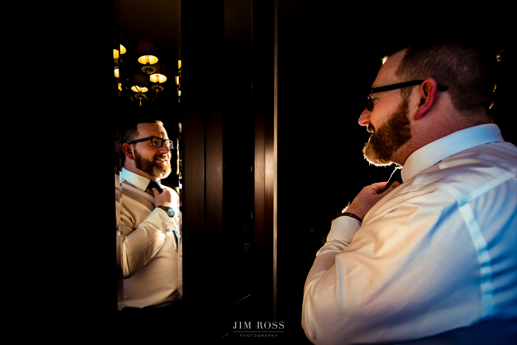 groom adjusts tie in mirror