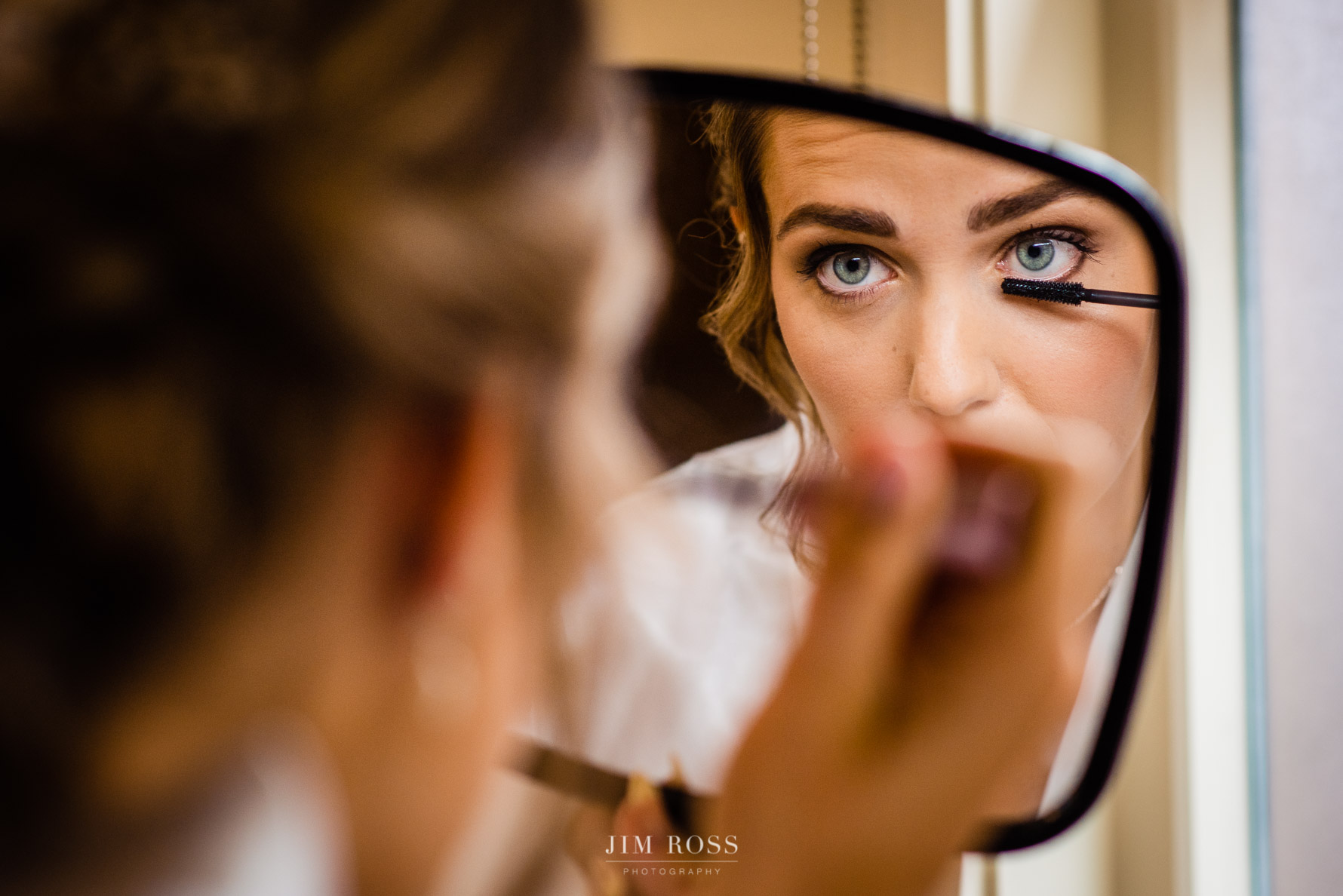 bride applies eye liner in mirror