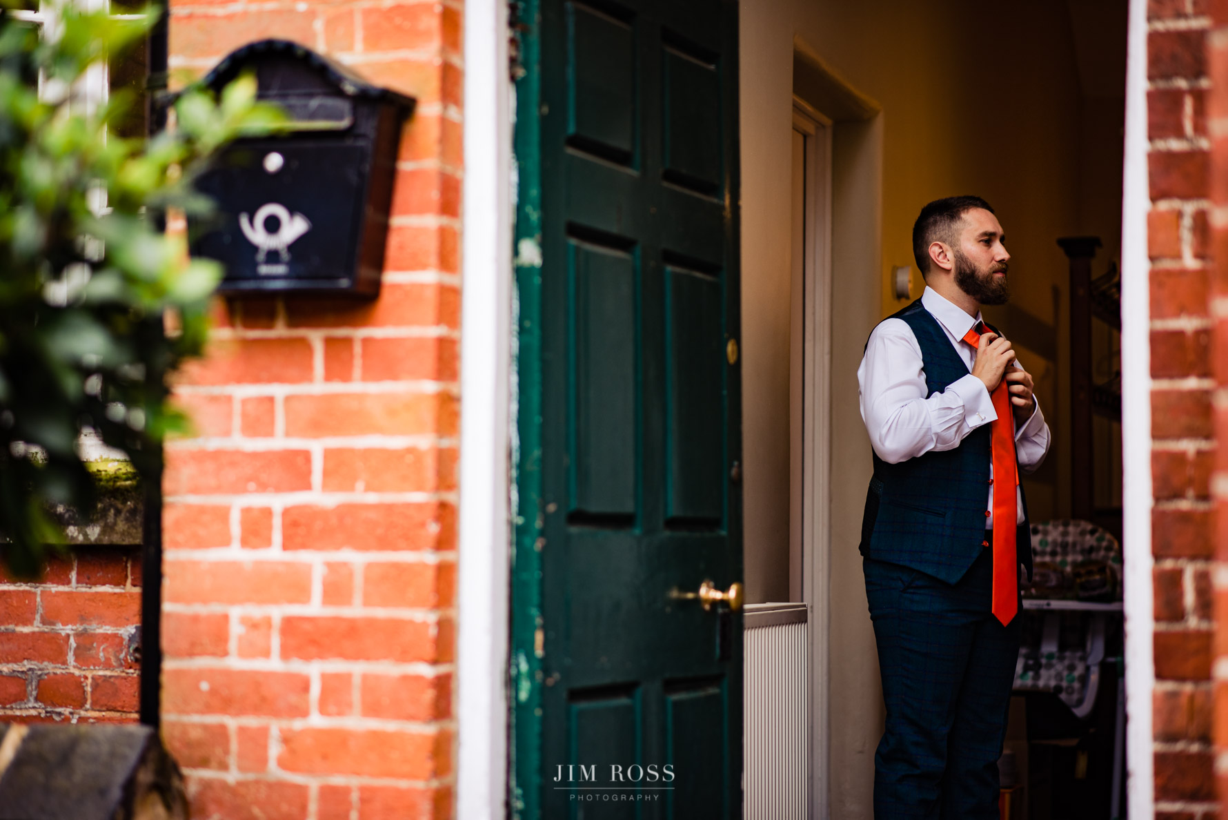 groom adjusts tie in doorway