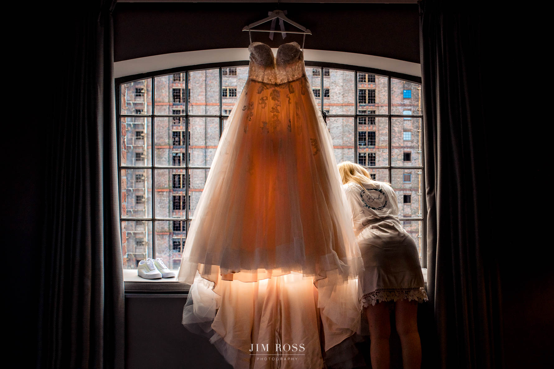 bride looks out of window behind hanging dress