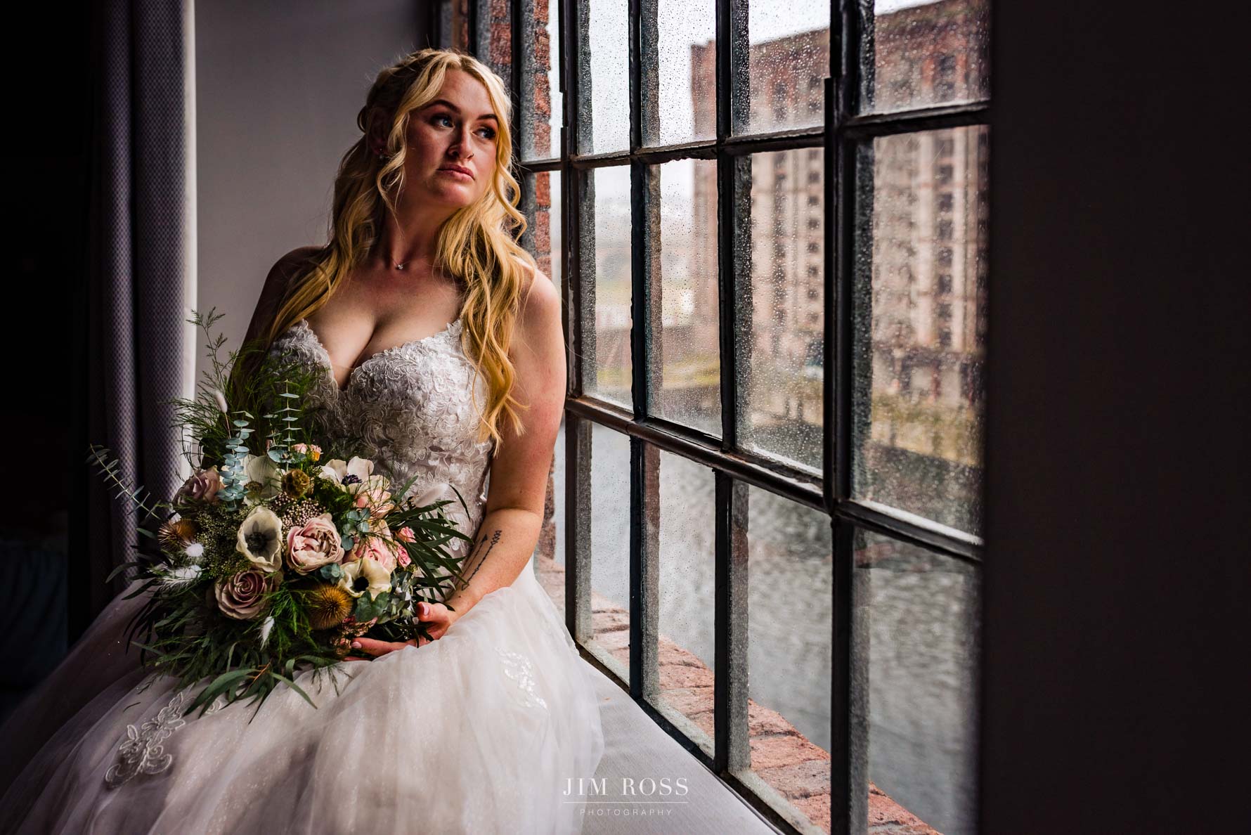 Bride ready with flowers sat in rainy window